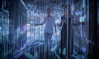 Zwei Personen laufen durch einen Vorhang aus hunderten von dünnen Fäden, auf den Lichtbilder projiziert werden